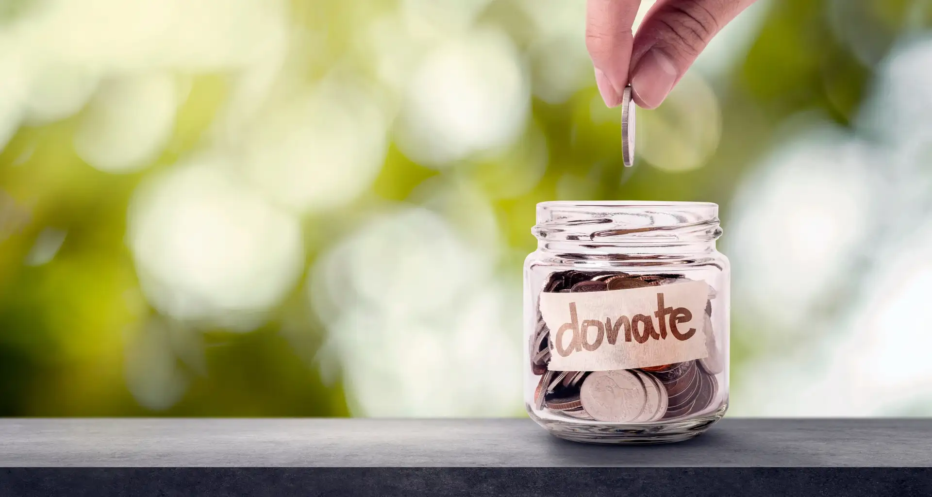 A hand dropping a coin into a jar labeled 'donate'